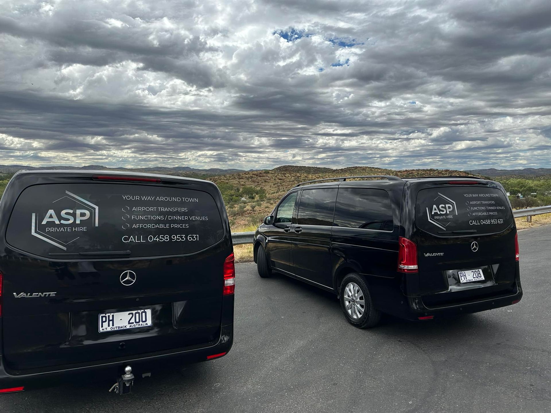 Two Black Vans Parked on a Cloudy Roadside With Desert Hills in the Background — ASP Private Hire in Ross, NT