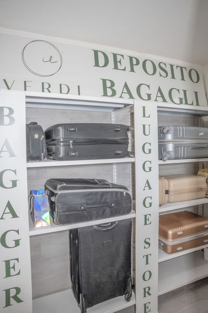 Scaffali per il deposito bagagli con valigie e borse in un'area di deposito, etichettata “DEPOSITO BAGAGLI” e “LUGGAGE STORAGE”