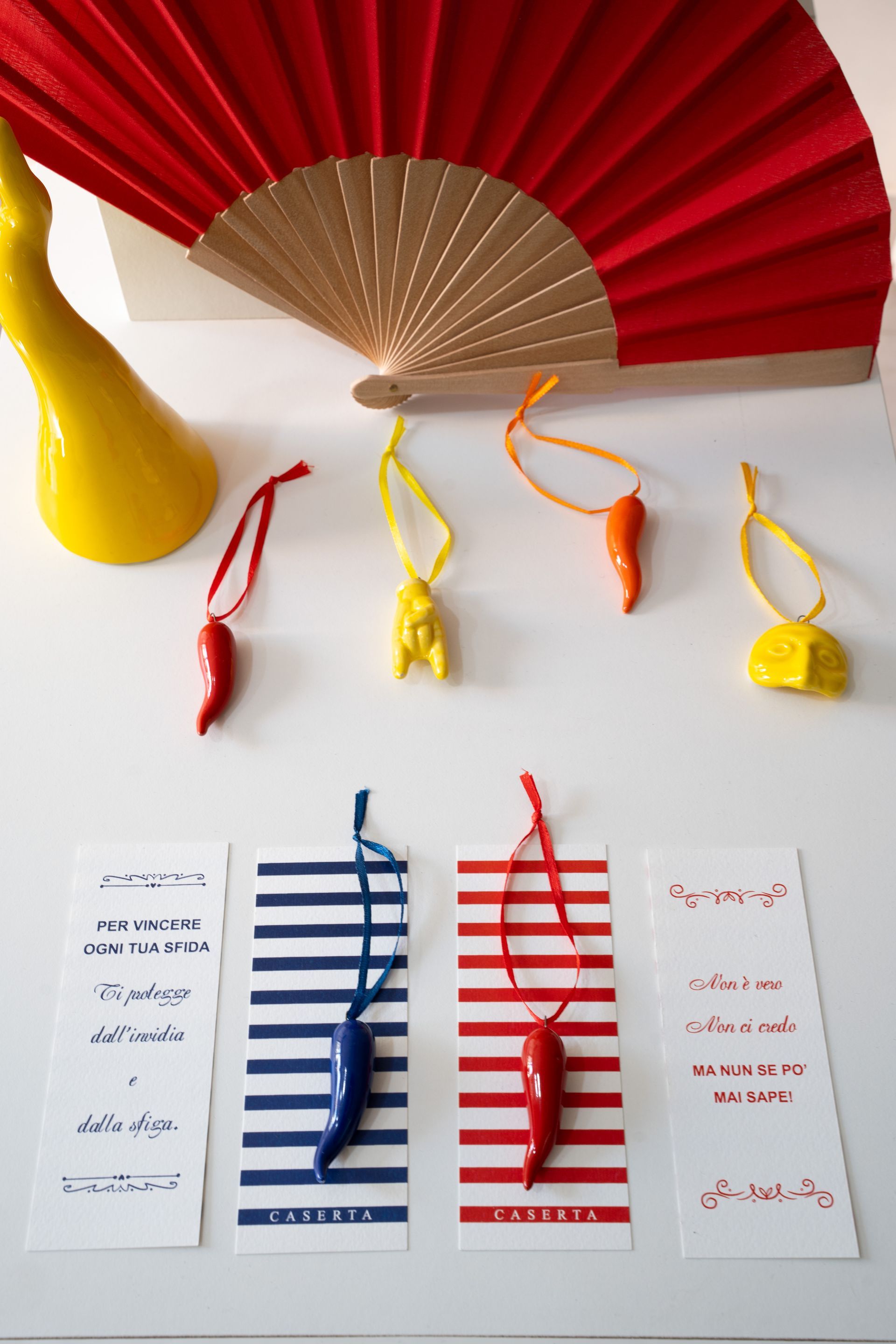 Ventaglio di carta colorato e nappe pendenti sopra cartoncini a righe su una superficie bianca.