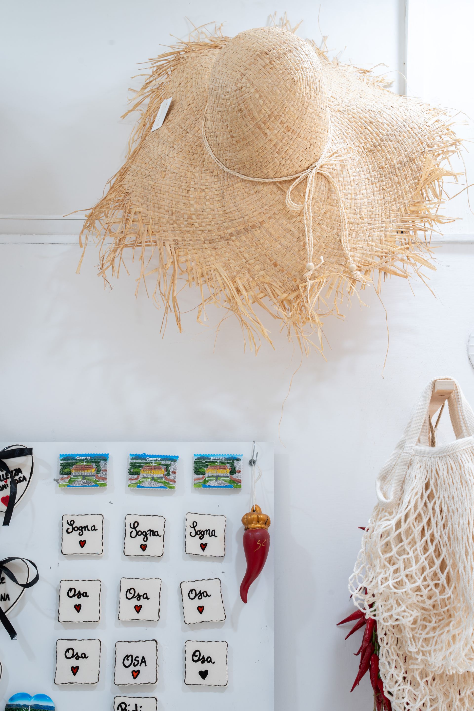 Decorazione da parete con un cappello di paglia intrecciata, piccoli cartoncini decorativi e una borsa a rete appesa con nappe rosse.