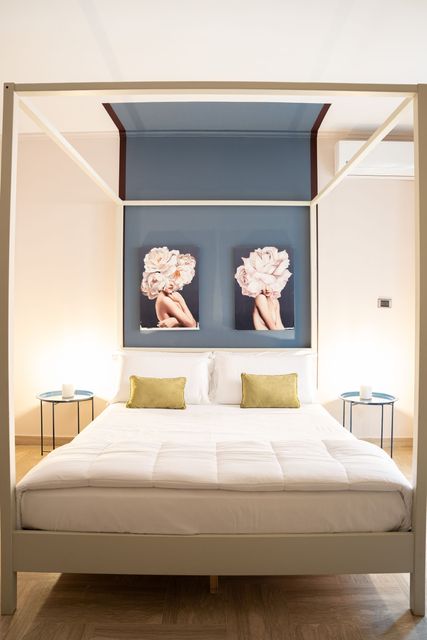 Camera da letto moderna con letto a baldacchino bianco, parete d'accento blu e quadro floreale sopra la testiera.