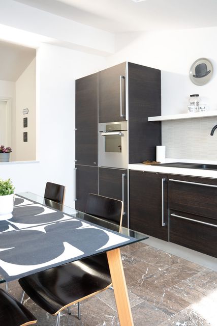 Cucina moderna con mobili scuri, frigorifero nero e tavolo da pranzo in primo piano.