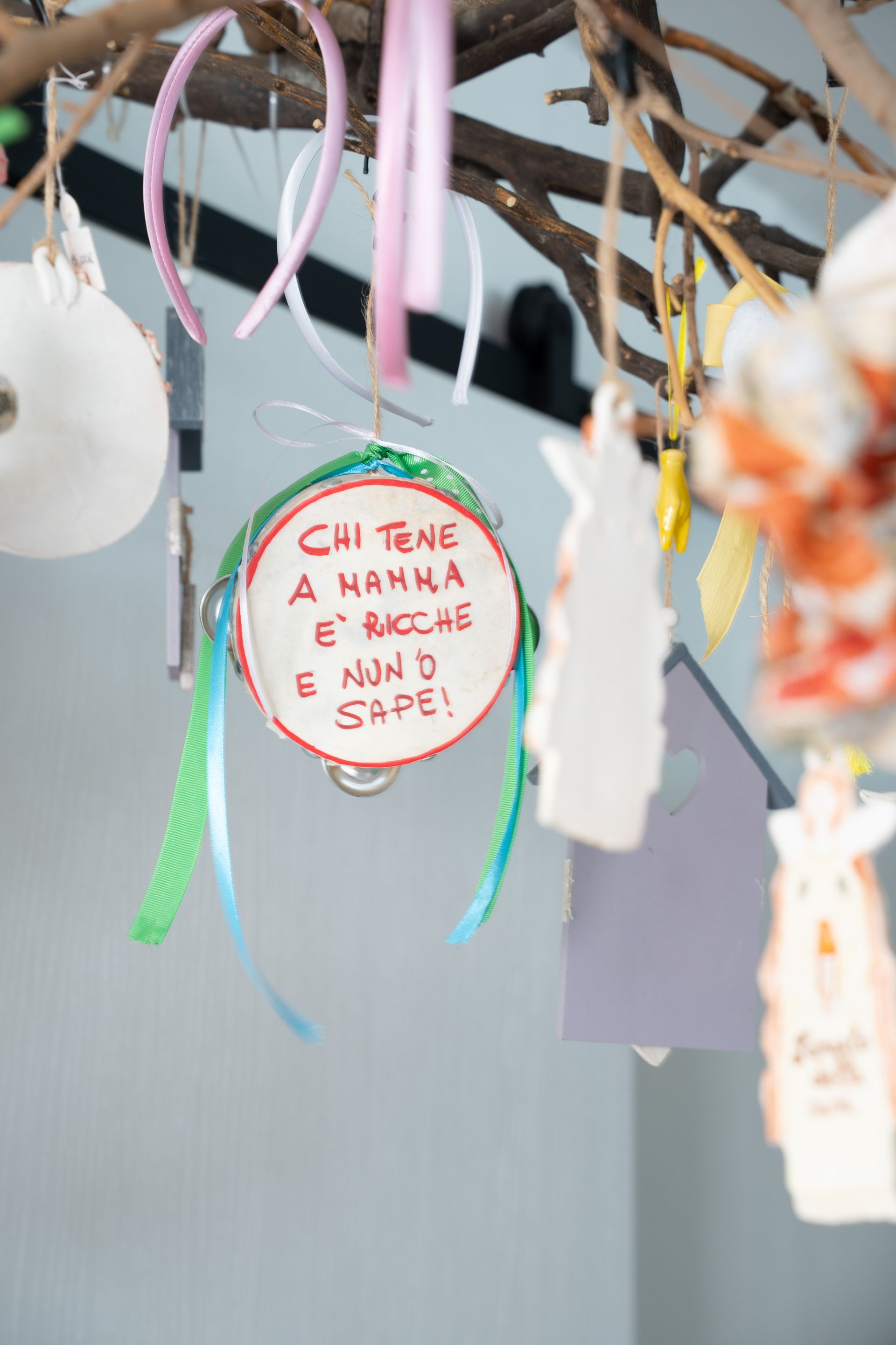 Ornamenti colorati da appendere, con un cartellino rotondo bianco recante una scritta rossa a mano, sospesi ai rami.