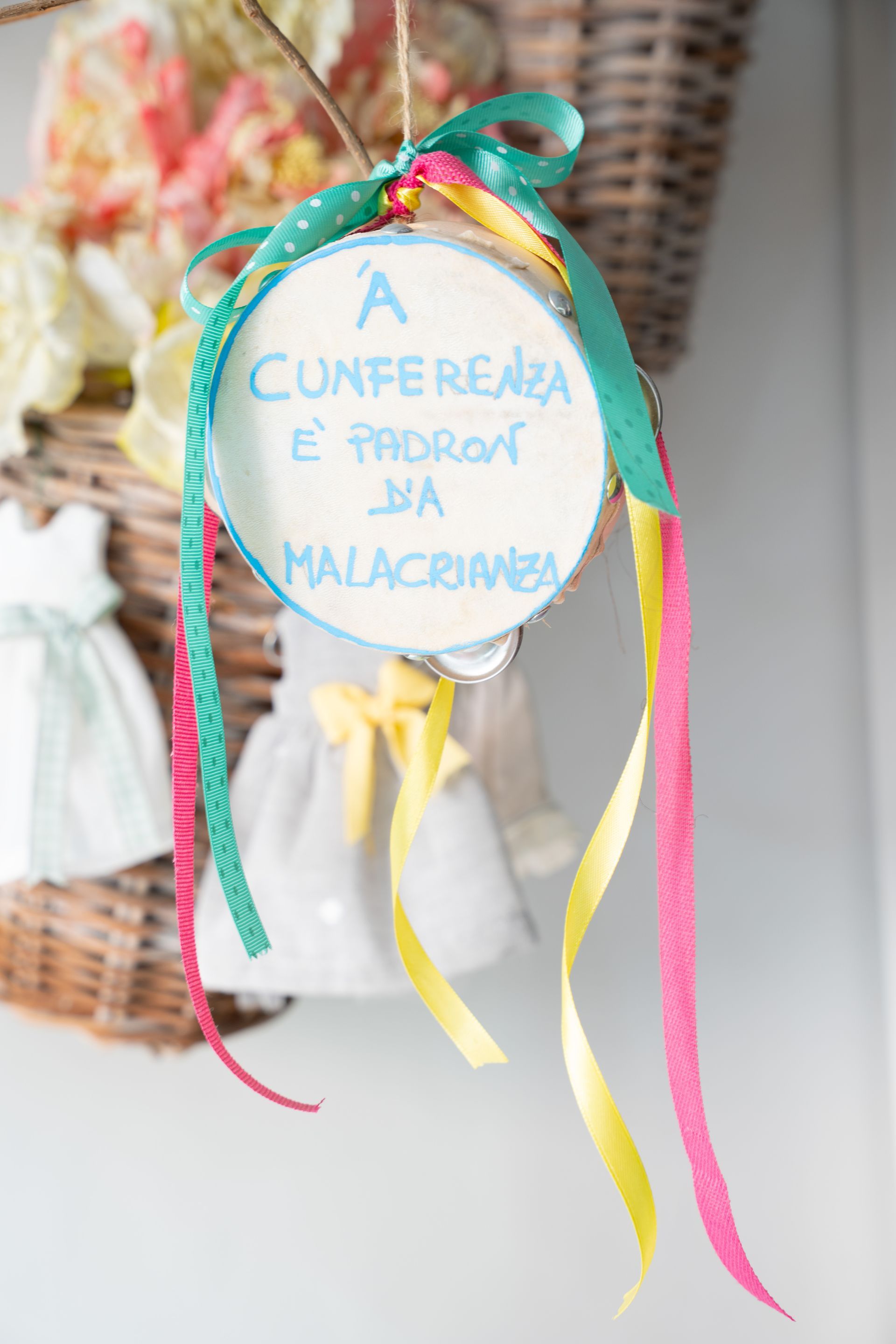 Cartello rotondo blu con nastri turchesi e multicolori con la scritta “A CUNFERENCIA é PROXIMA DIA 1MAIO”