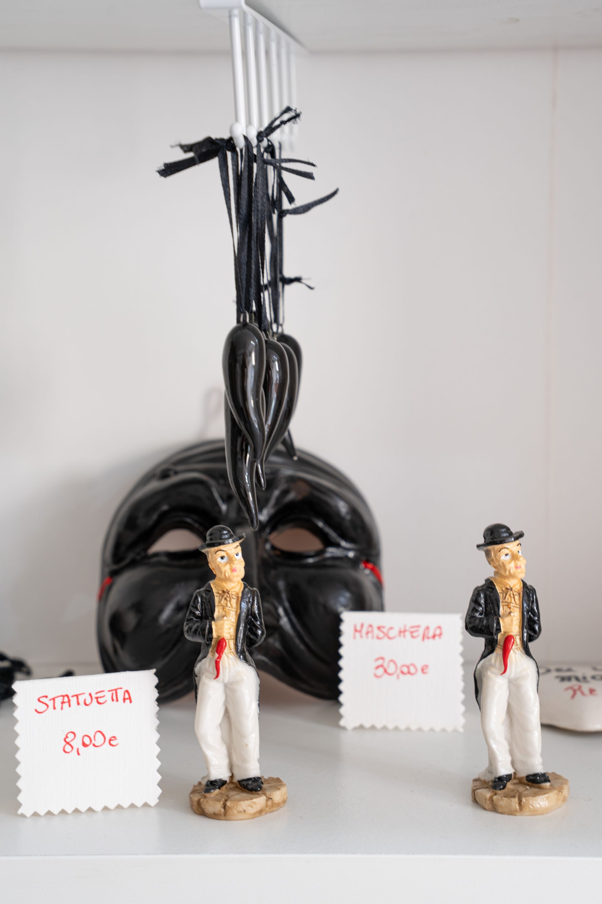 Due piccole statuine in uniforme bianca si ergono davanti a una scultura nera con cartellini dei prezzi scritti a mano.