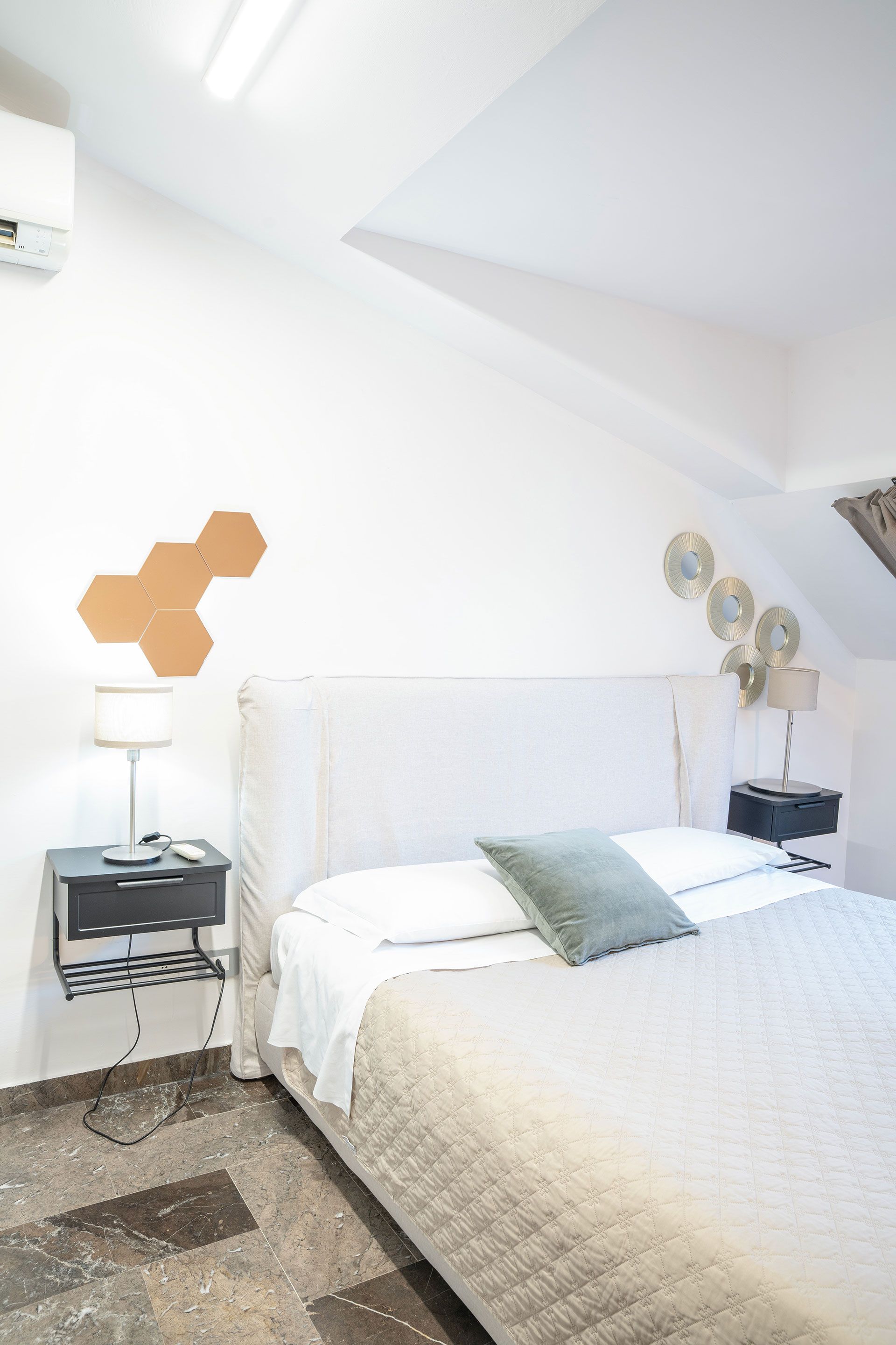 Camera da letto luminosa e bianca con letto, comodino e soffitto inclinato.