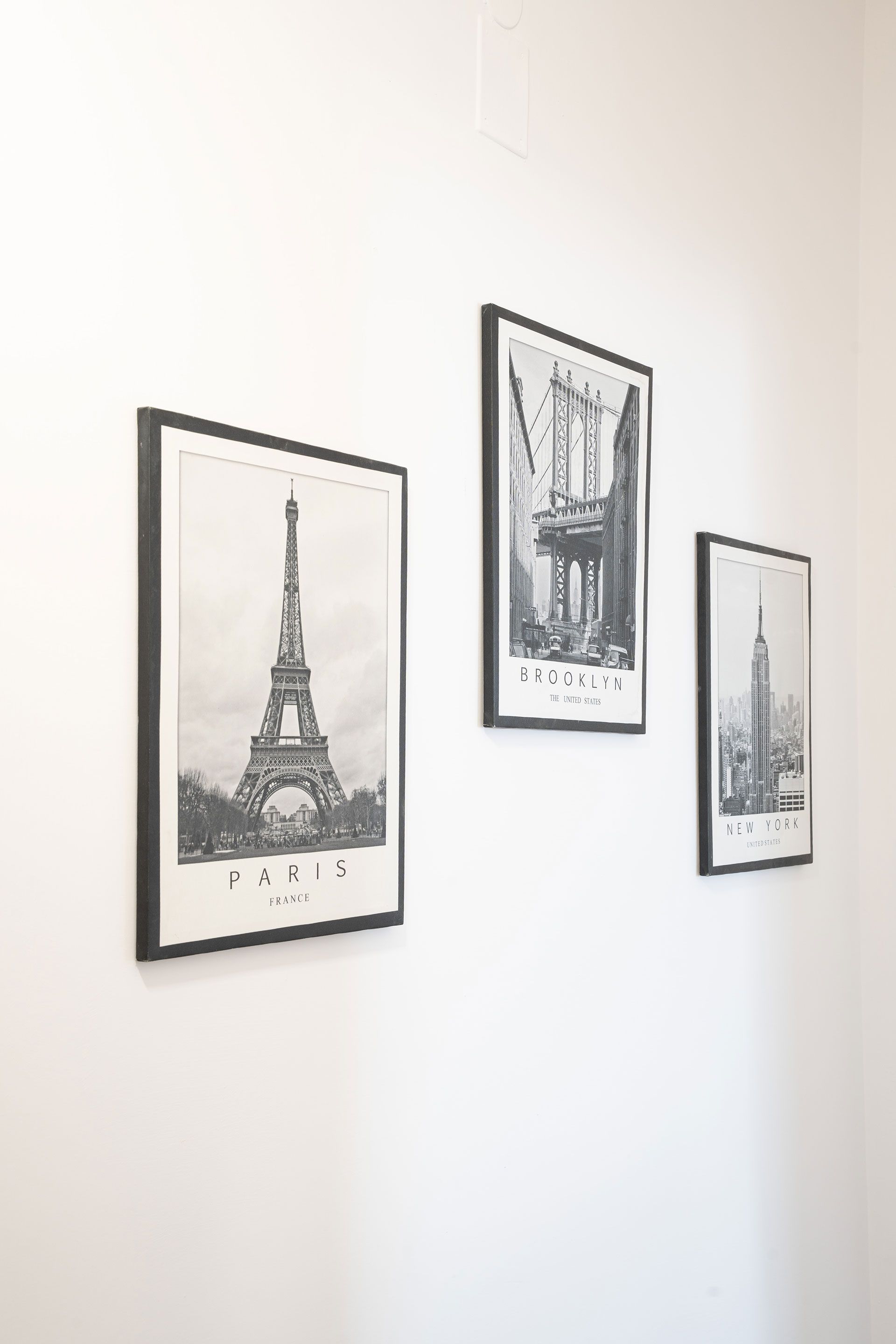 Tre stampe in bianco e nero di città, tra cui la Torre Eiffel, incorniciate e appese a una parete bianca.