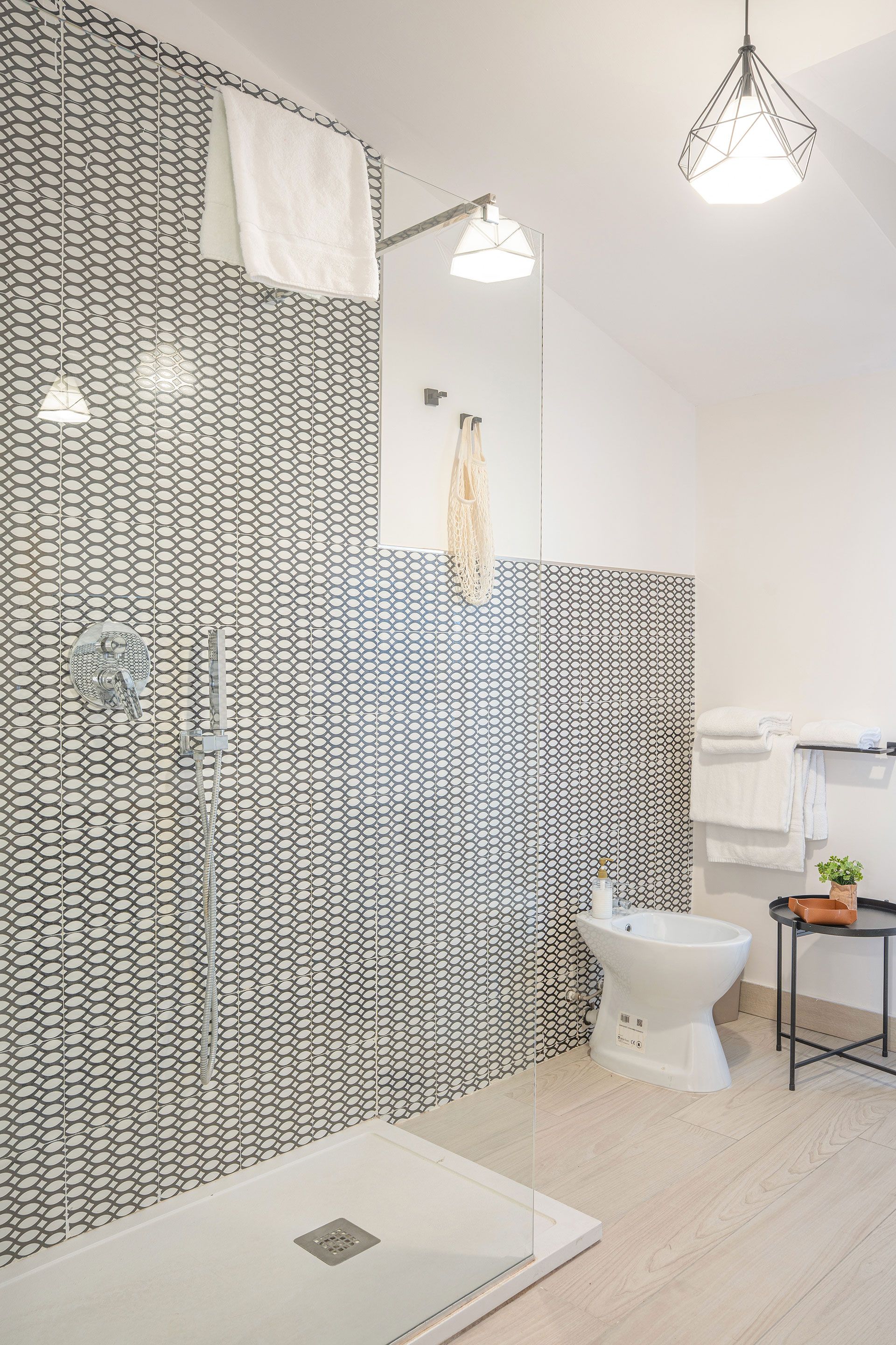 Bagno moderno piastrellato con WC bianco, zona doccia e pavimento e rubinetteria in legno chiaro.
