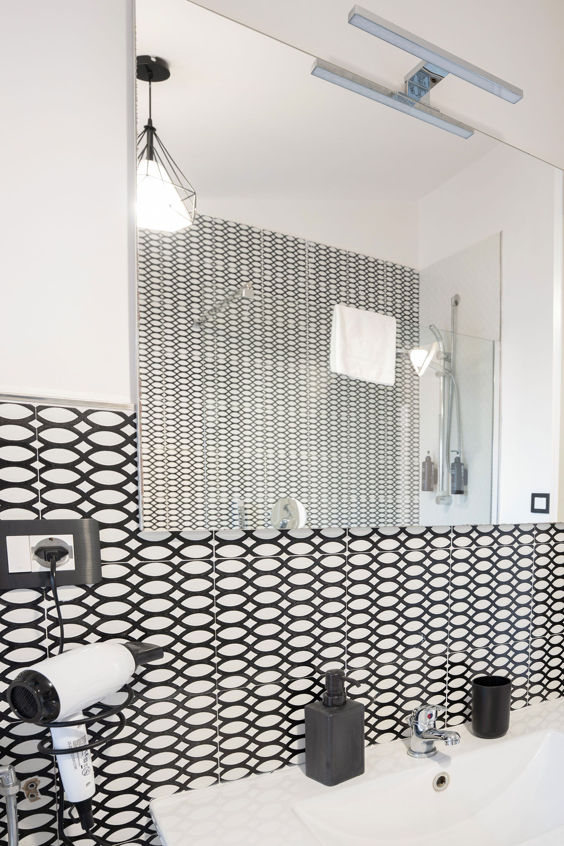 Bagno moderno con piastrelle decorate in bianco e nero, specchio, lavabo e applique a parete.