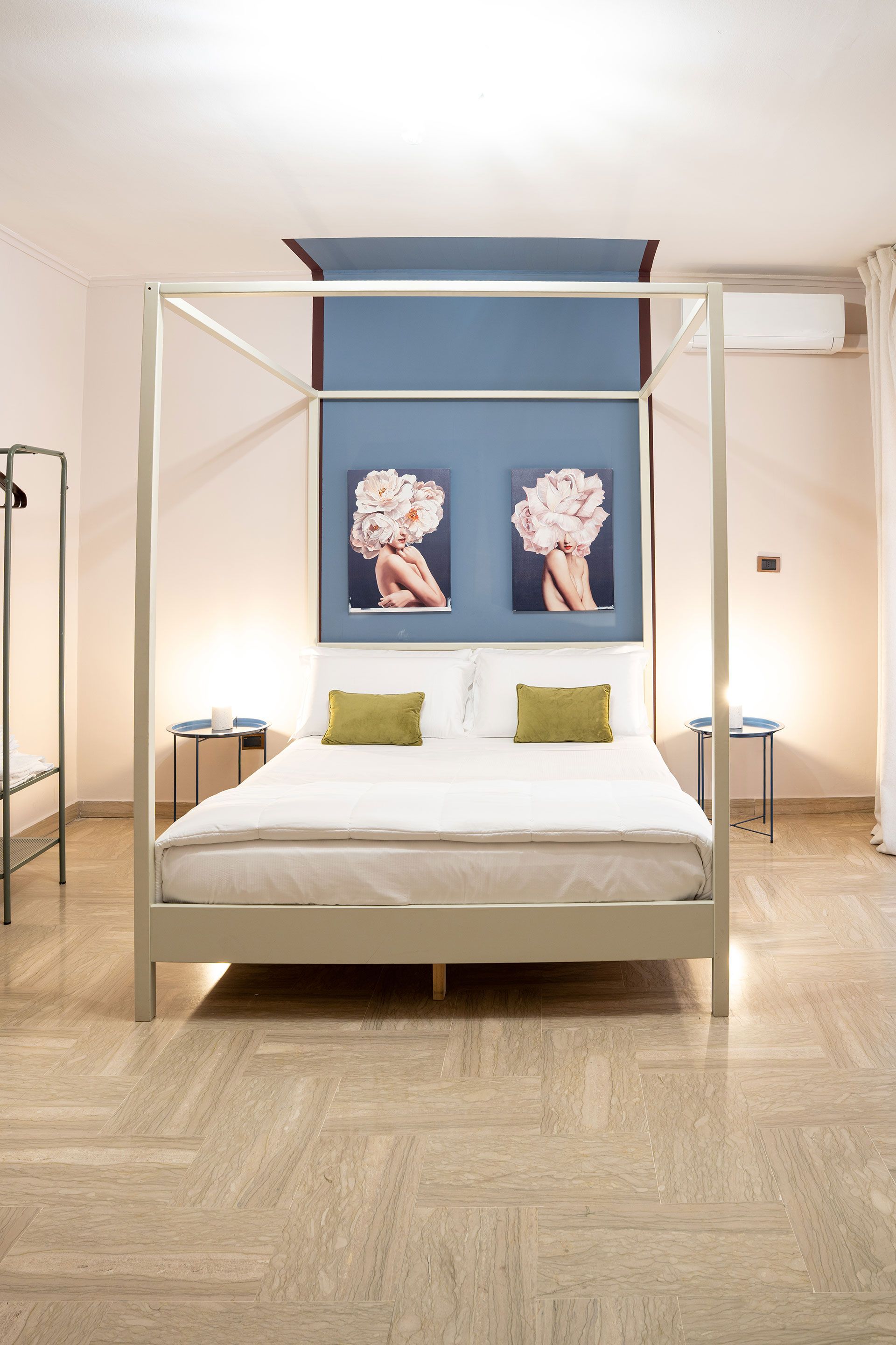 Camera da letto moderna con letto a baldacchino bianco, parete d'accento blu e due stampe floreali incorniciate sopra la testiera.