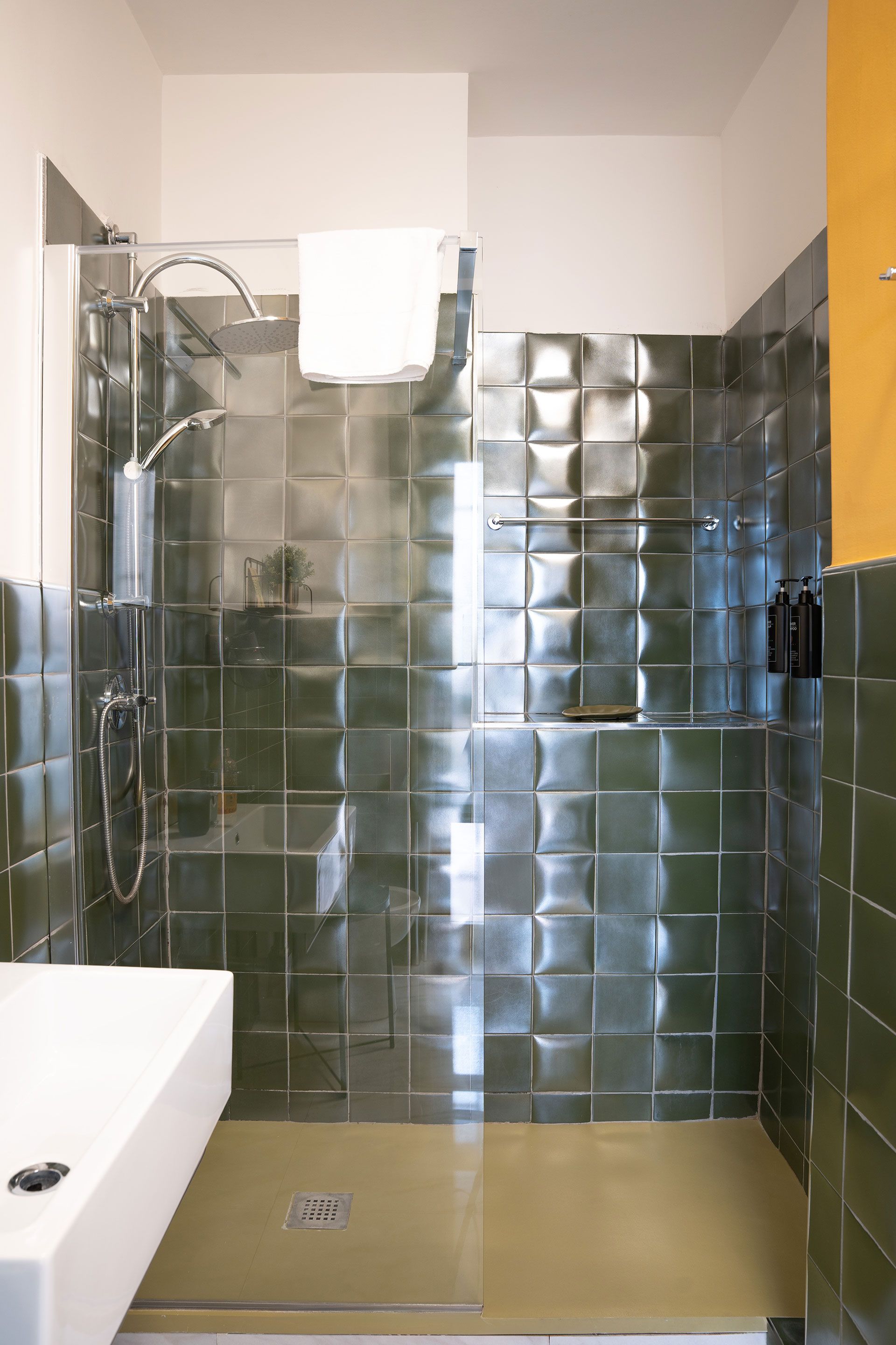 Piccolo bagno con doccia e vasca rivestite di piastrelle verdi, pavimento beige e pareti bianche.
