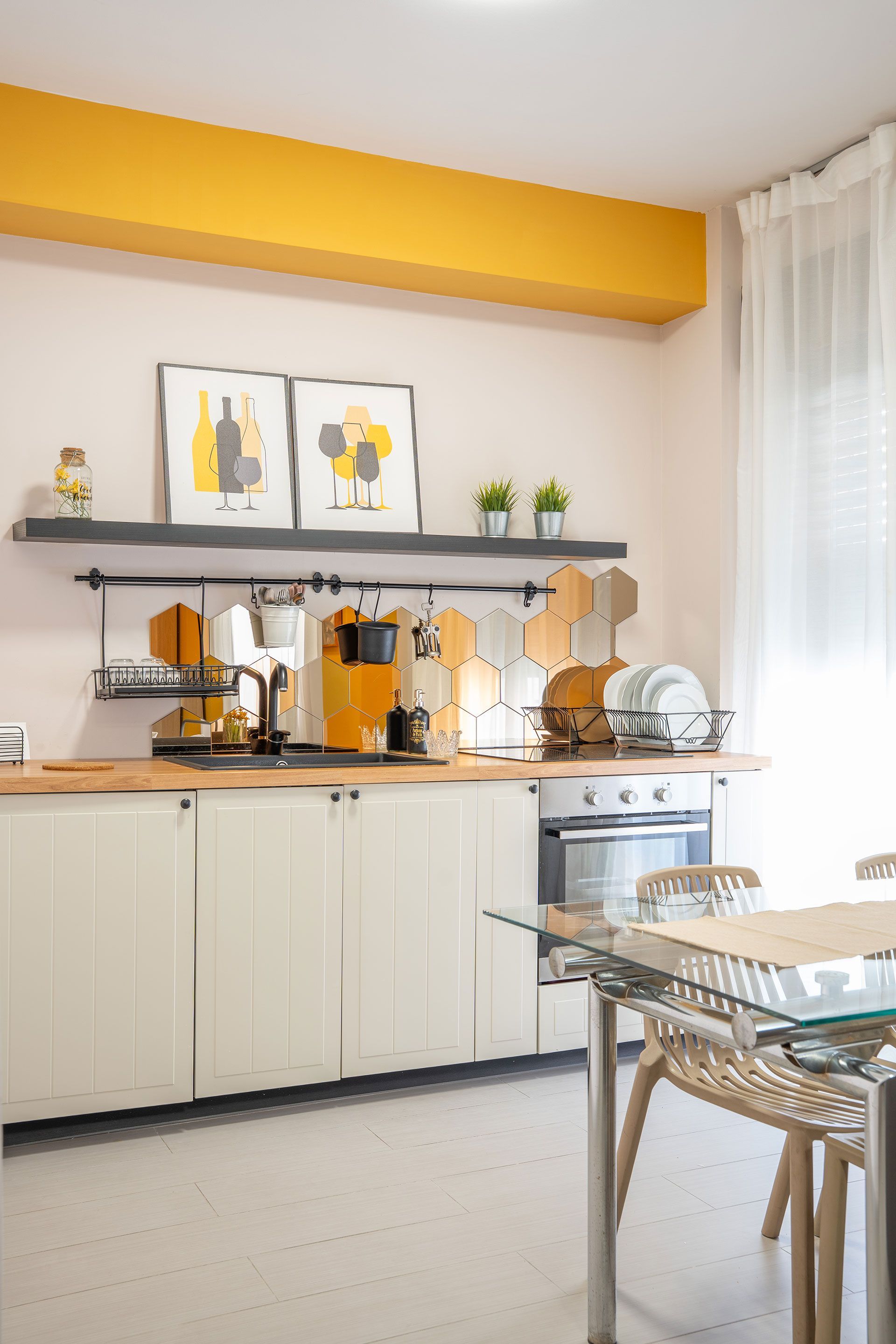 Luminoso angolo cucina con mobili bianchi, dettagli arancioni, mensole e un piccolo tavolo da pranzo vicino a una finestra.