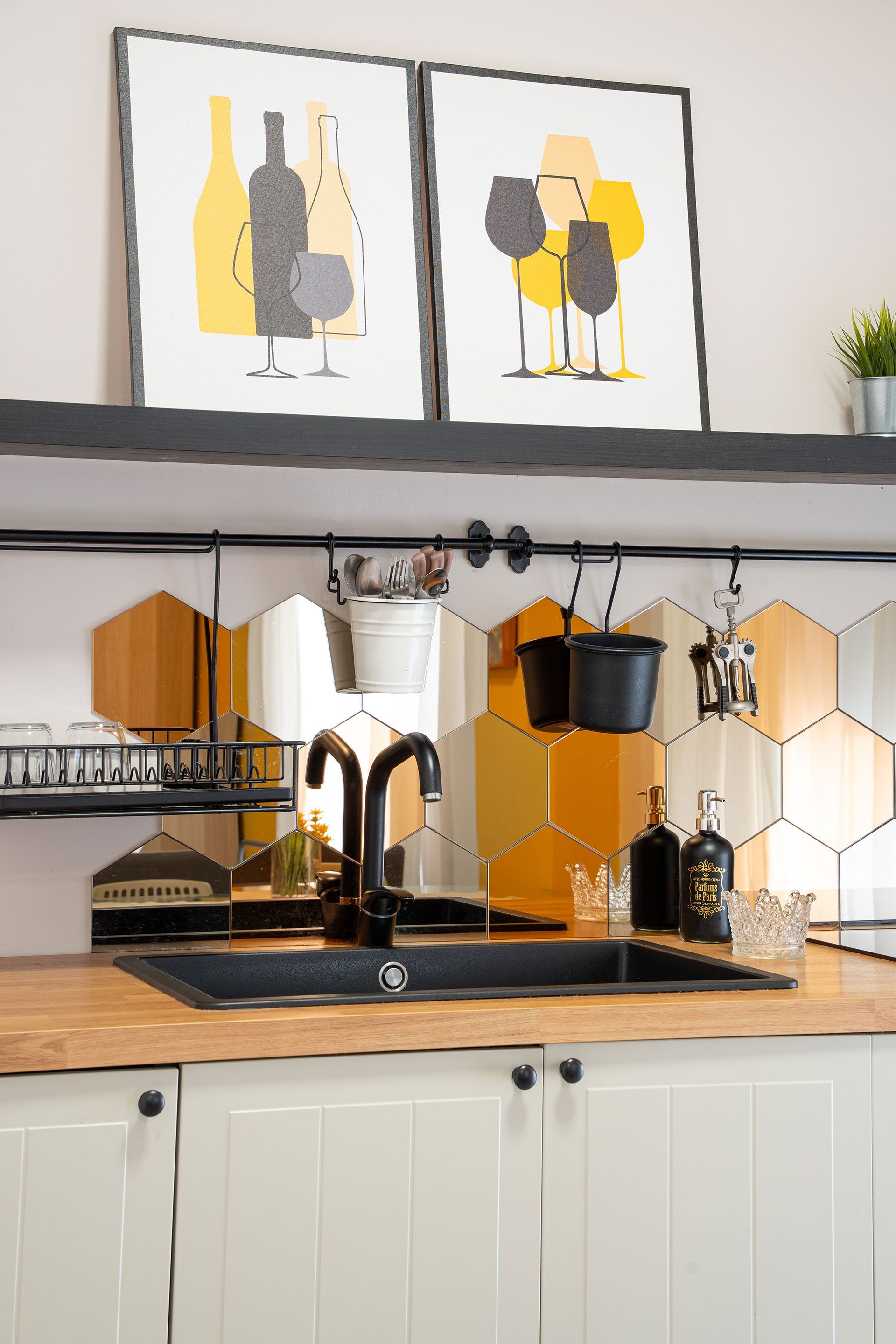 Bancone da cucina moderno con macchina da caffè nera e oro, paraschizzi in piastrelle esagonali e quadro astratto incorniciato sopra le mensole.