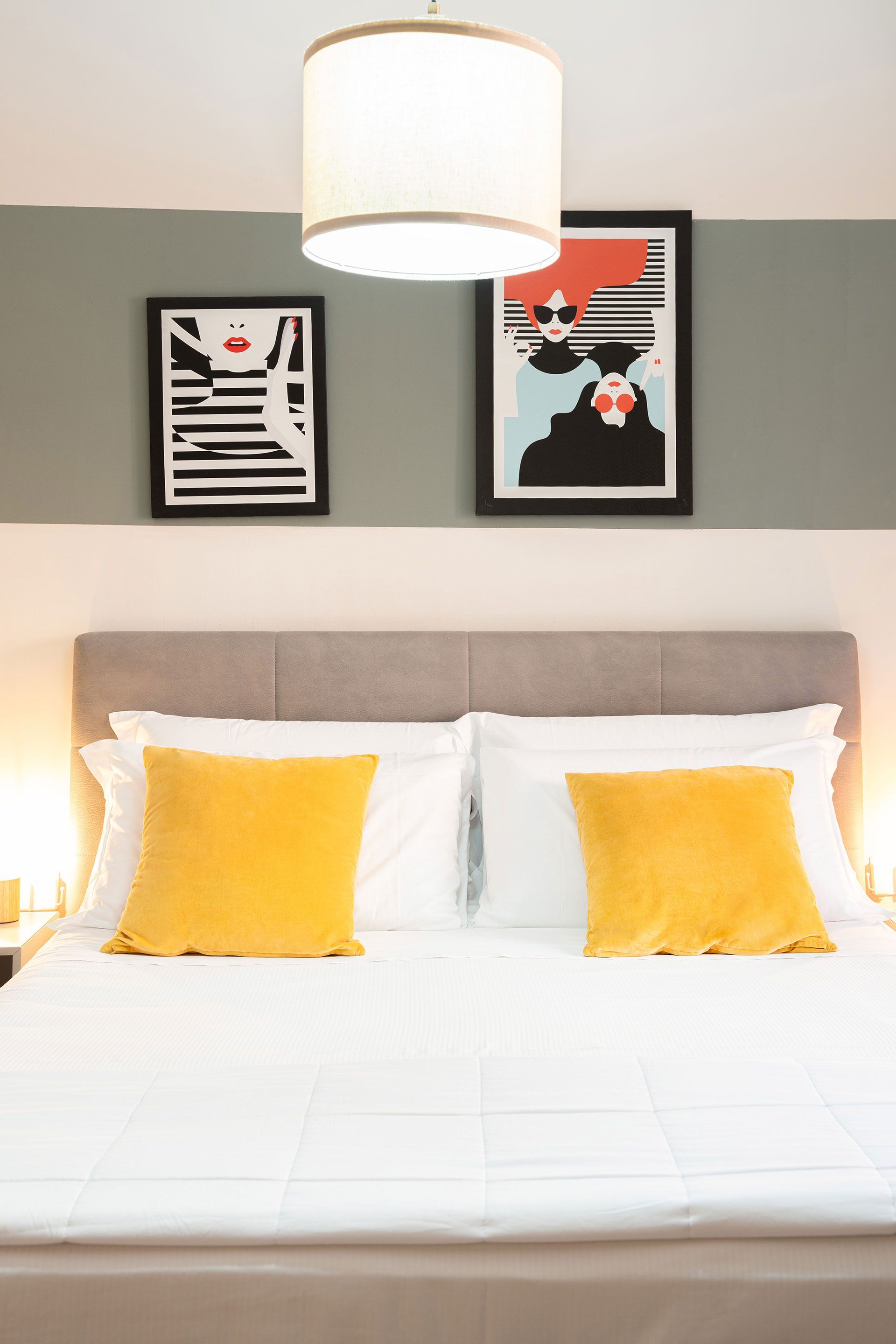 Camera da letto luminosa con letto bianco, cuscini gialli e quadro incorniciato sopra la testiera.