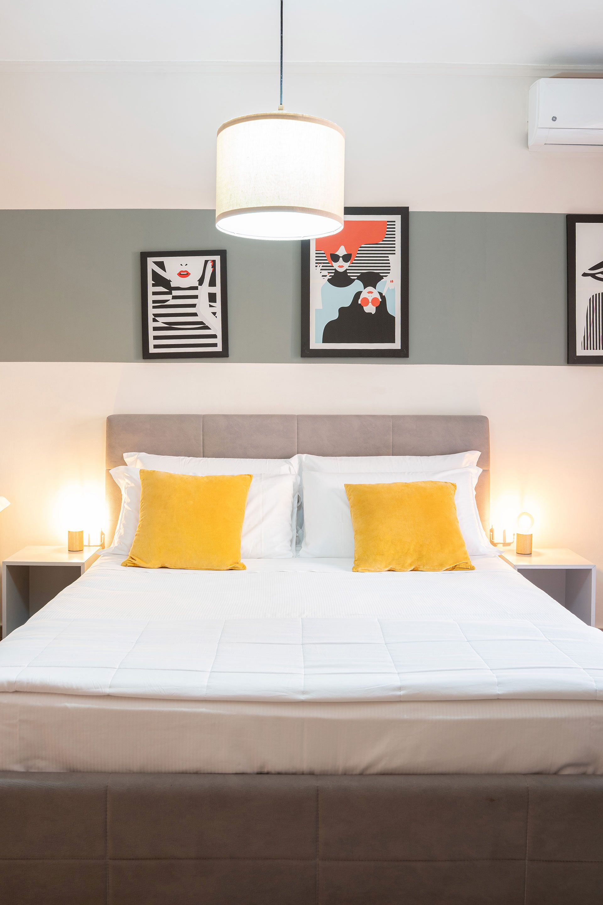 Camera da letto moderna con letto ben rifatto, cuscini gialli, lampade da comodino e quadri appesi alle pareti.