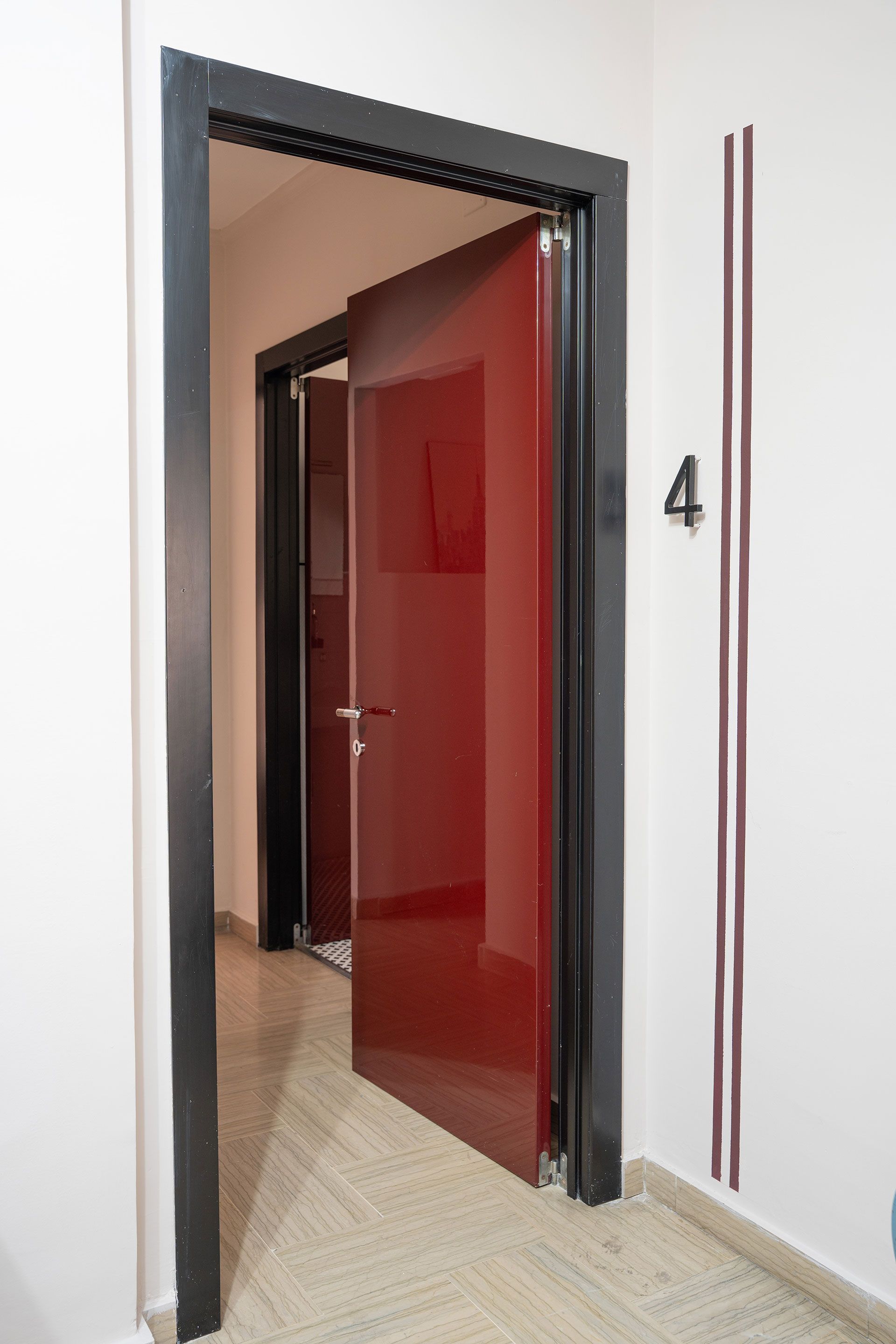 Porta aperta con anta in vetro rosso e cornice nera in un corridoio, contrassegnata dal numero 4.