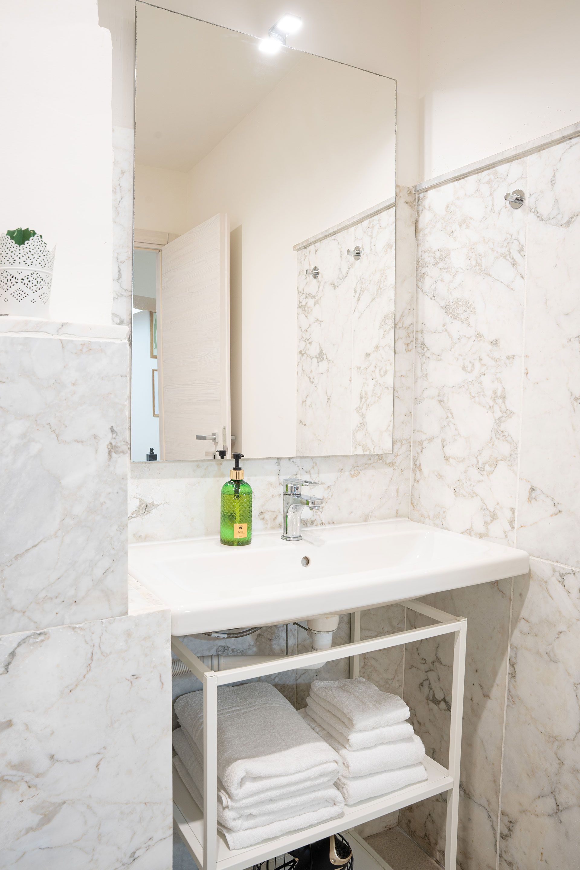 Moderno mobile da bagno in marmo bianco con specchio, lavabo, dispenser di sapone e portasciugamani piegati sottostante.