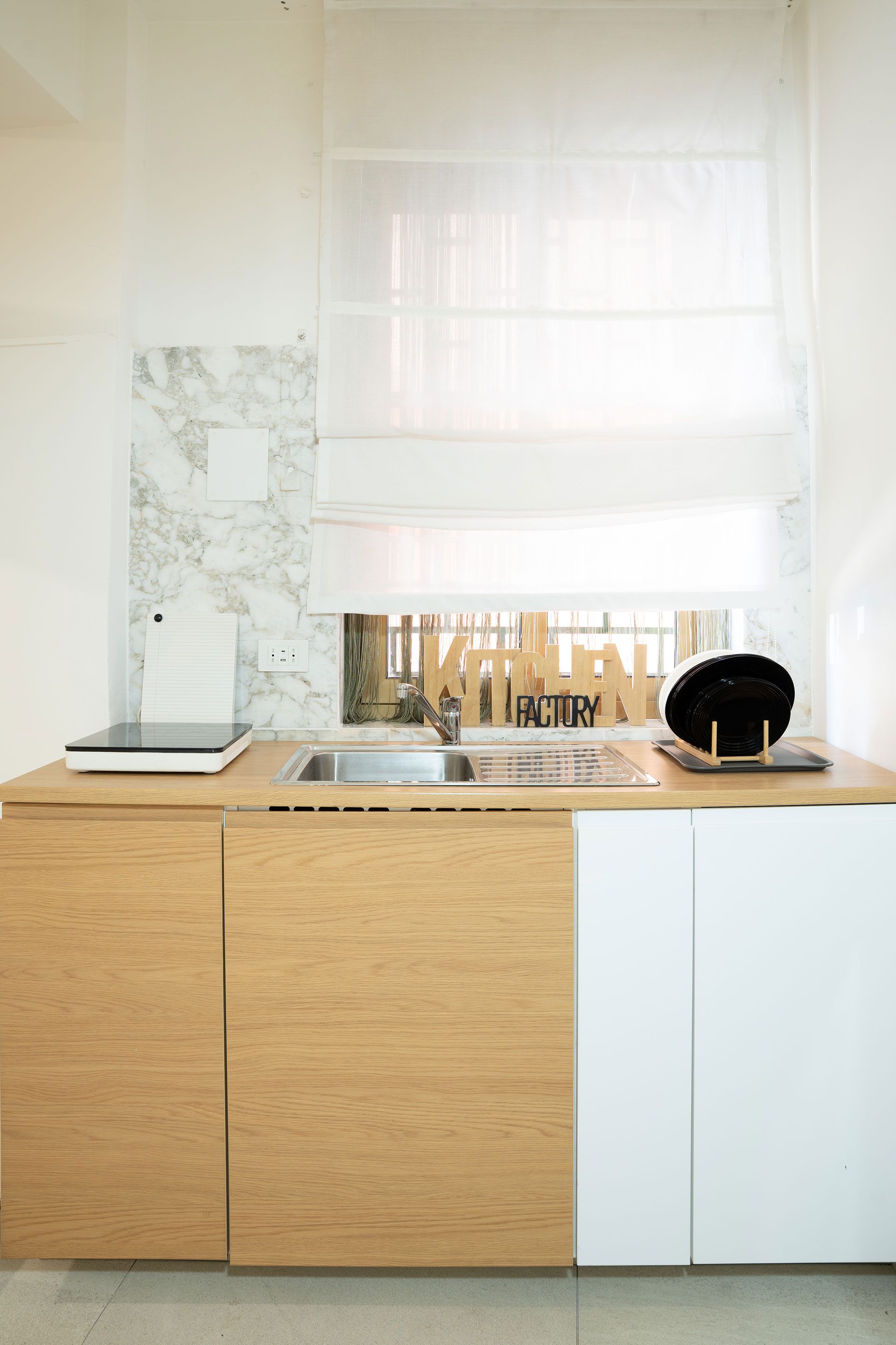 Cucina moderna con mobili in legno e bianchi, lavello, paraschizzi in marmo e una finestra sopra il bancone.
