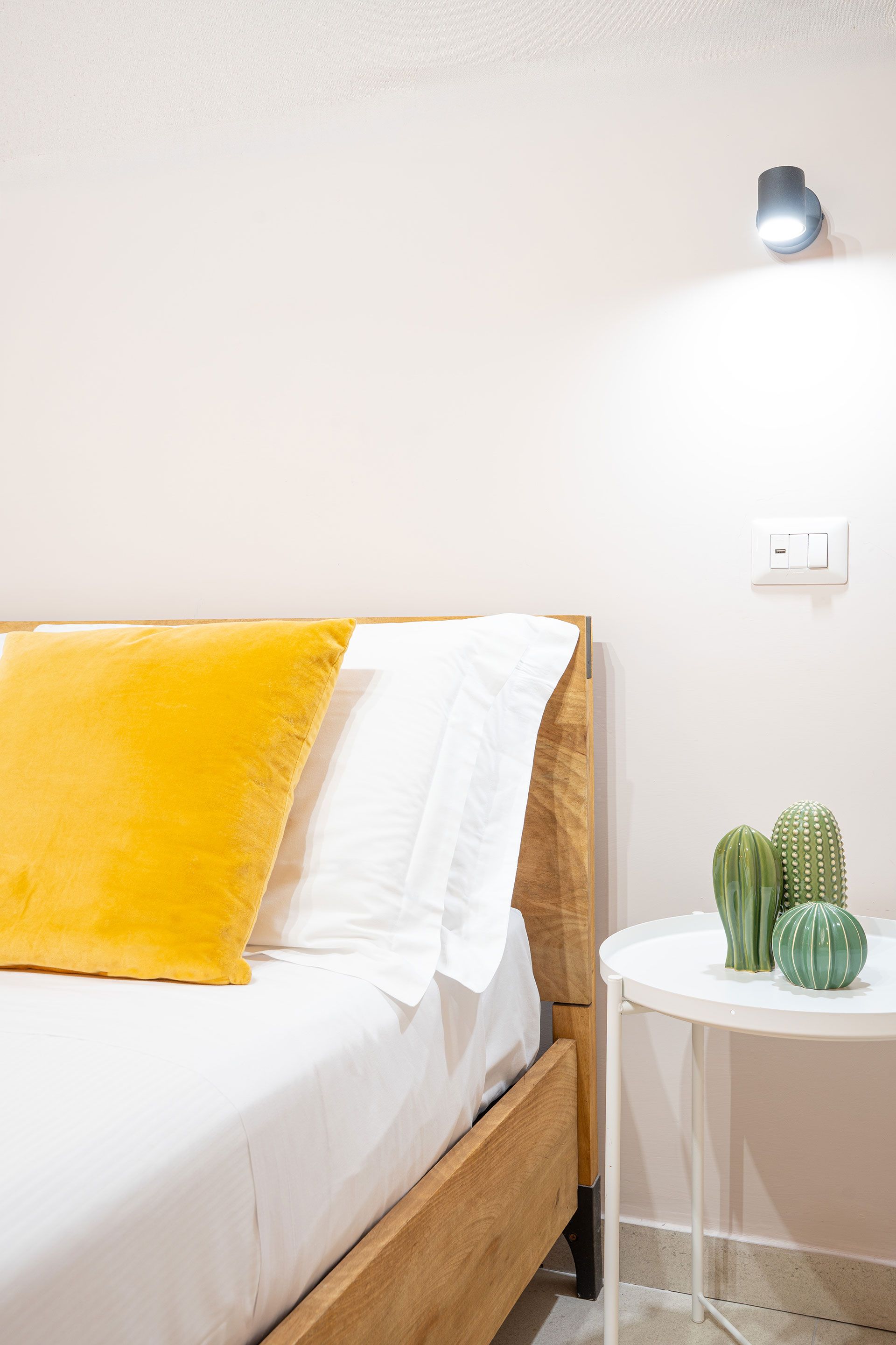 Luminoso angolo della camera da letto con lenzuola gialle, comodino bianco e piccoli cactus verdi.