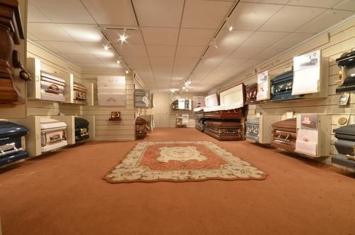 Wide showroom with display shelves, rugs, and flooring samples under bright ceiling lights.