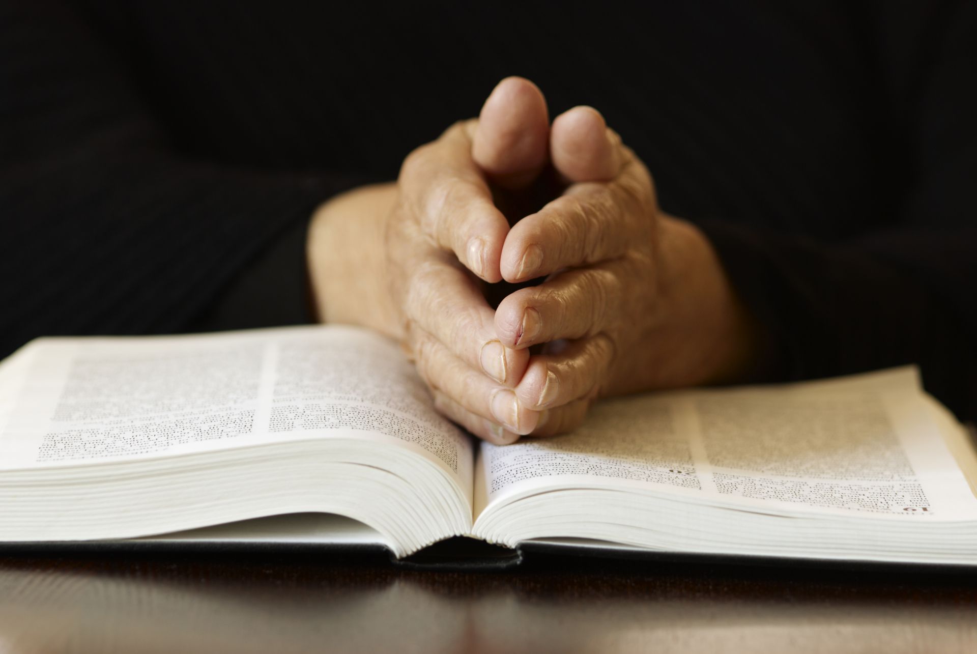Hands clasped in prayer above an open book on a table.