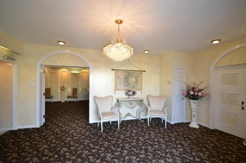 Elegant lobby with chandelier, white chairs, arched doorways, and patterned carpet