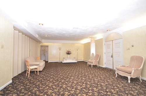 Spacious beige waiting room with patterned carpet, chairs along the walls, and a small table in the center