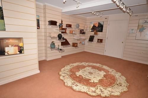 Small gallery room with white walls, display shelves, tan carpet, and a round rug in the center.