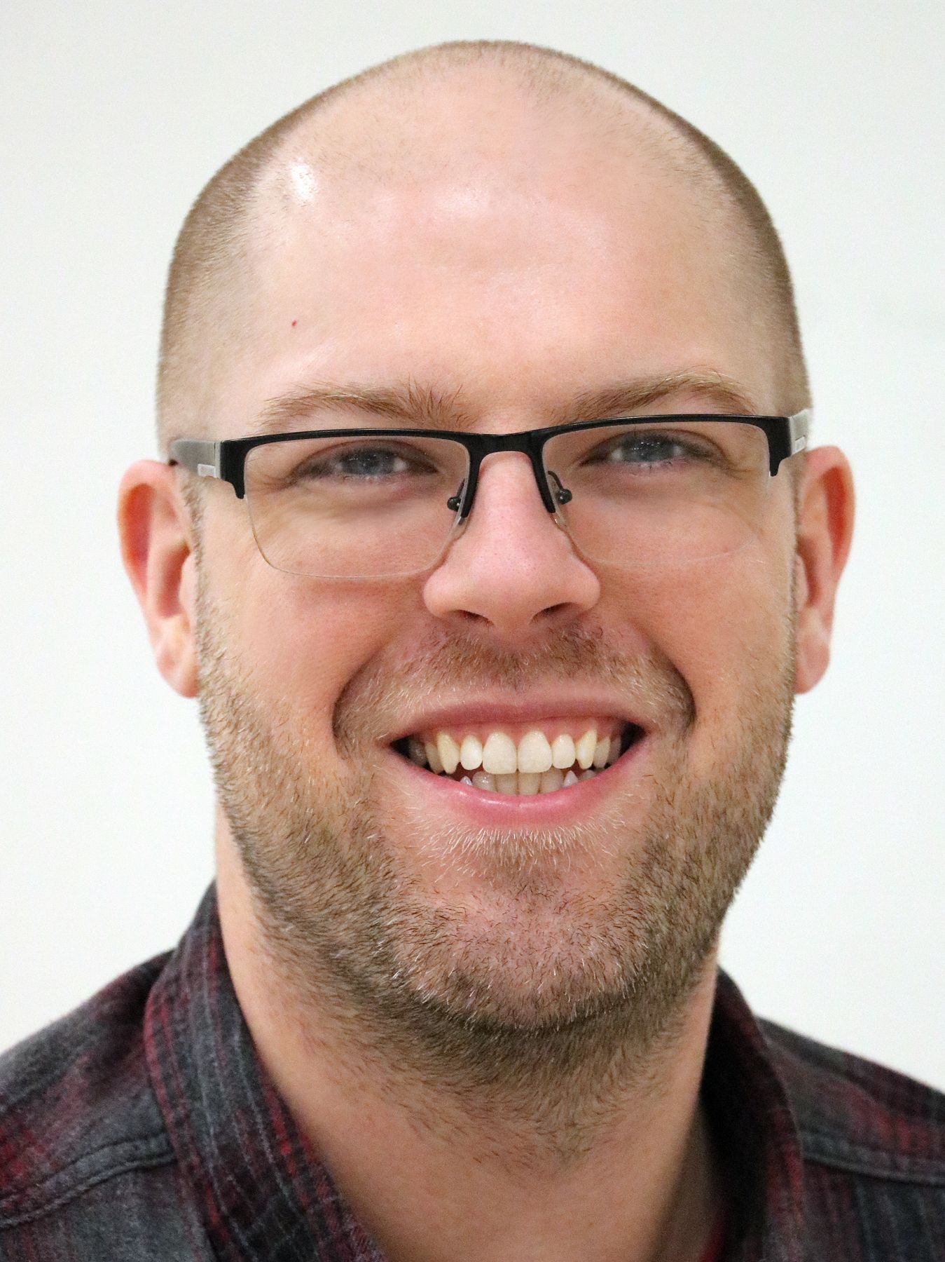 Smiling bald man with glasses and a plaid shirt against a light background