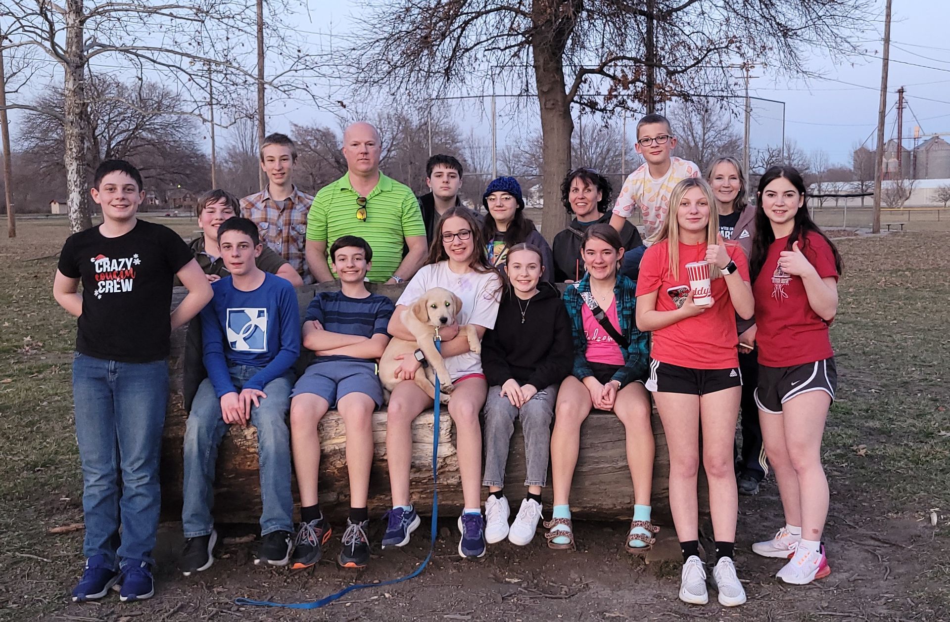 Group posing outdoors in casual clothes, with a seated woman holding a small dog at center.
