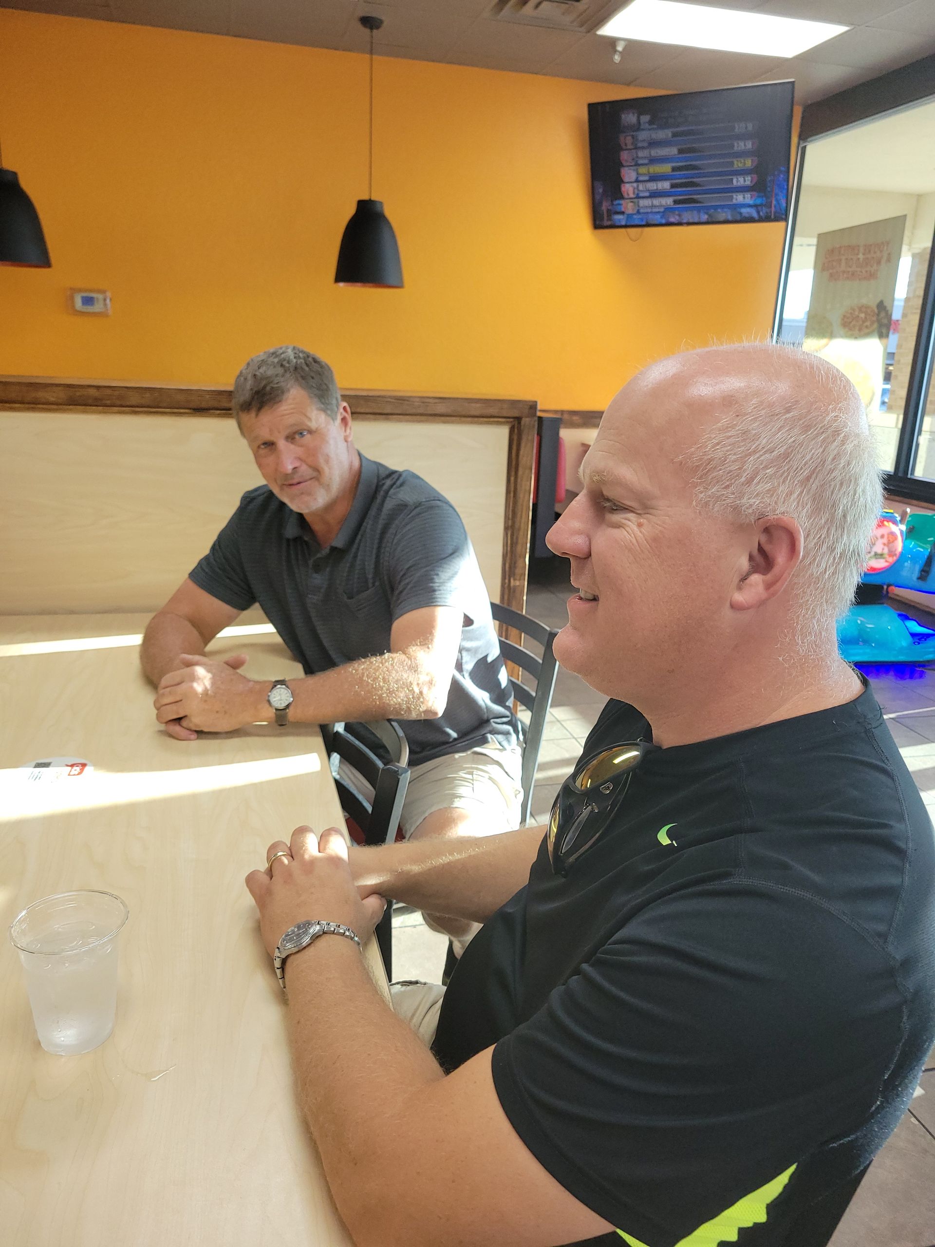 Two men sitting at a restaurant table, talking under warm yellow lighting.