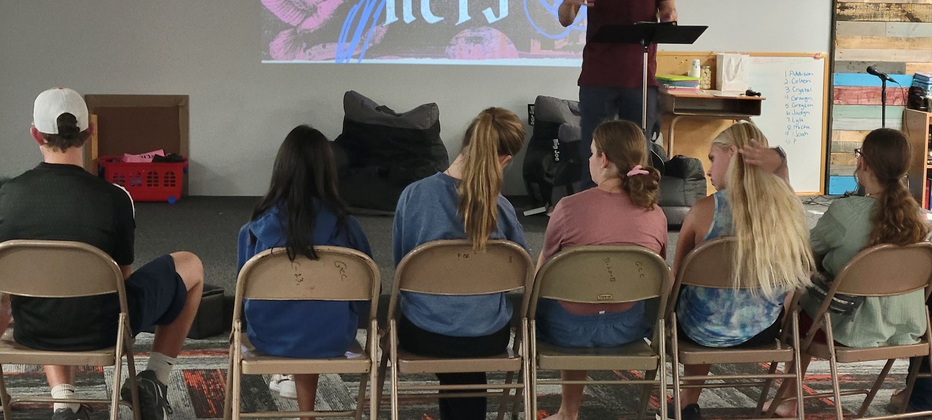 People seated in folding chairs watching a presentation on a screen indoors