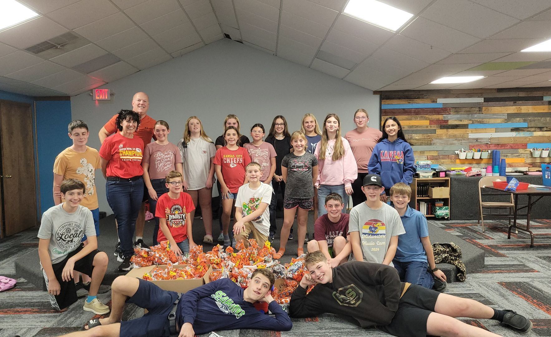 Group posing in a library, many wearing red shirts, with bookshelves and colorful book display behind them