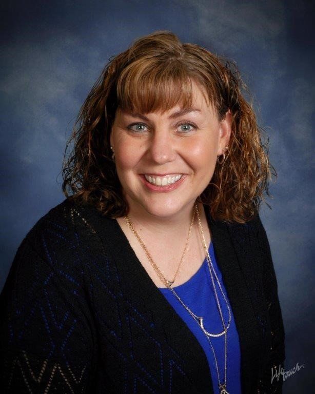 Smiling woman in blue top and black sweater against a dark studio backdrop