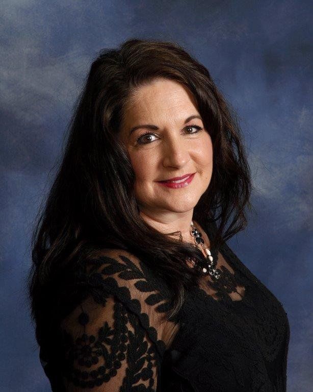 Studio portrait of a smiling woman with dark hair in a black lace top against a blue backdrop