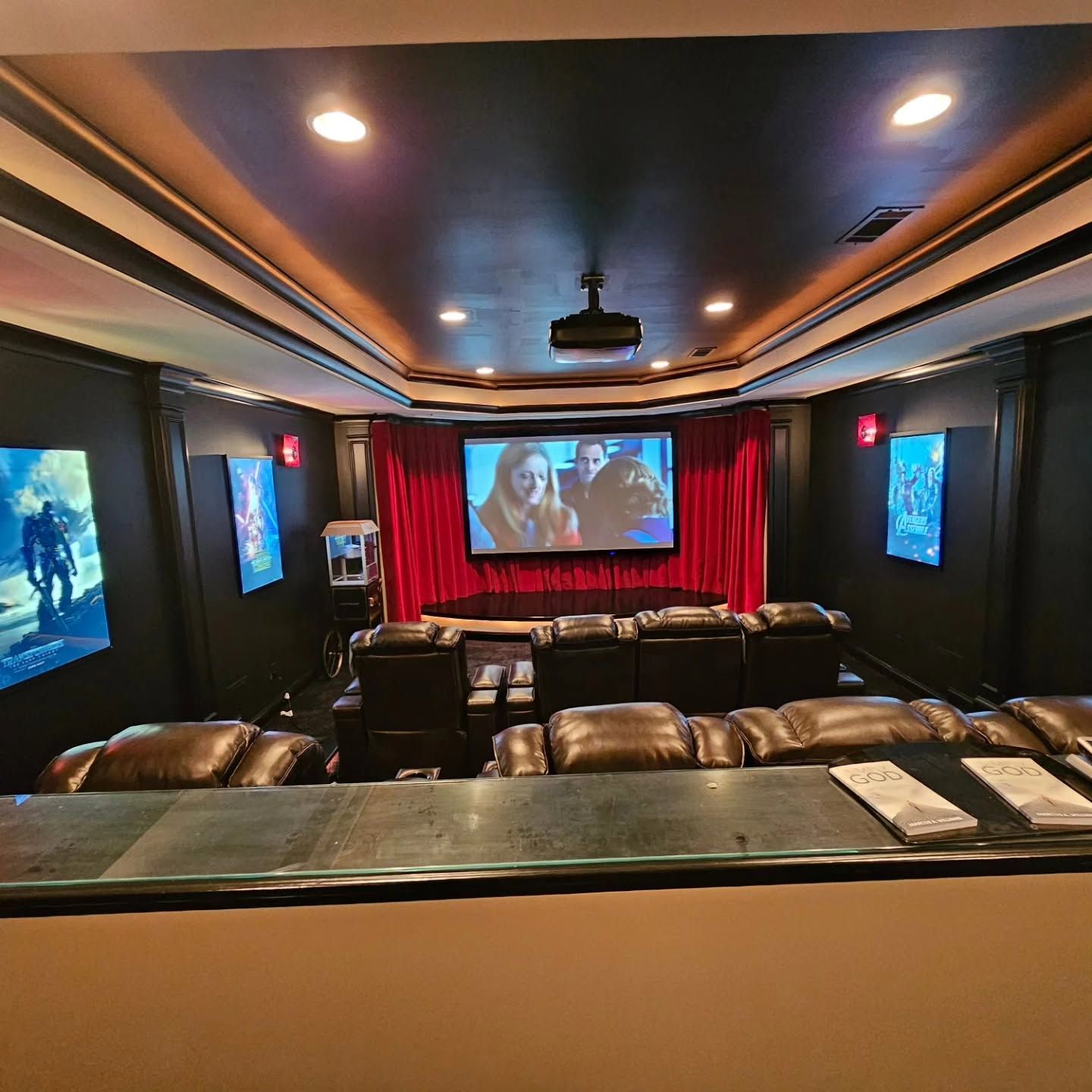Home theater with leather seats, red curtains, and a movie playing on a large screen.