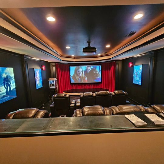 Luxurious home theater with leather seats, red curtains, and a movie playing on the screen