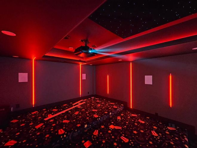 Red-lit empty room with dark patterned floor and ceiling fan, seen from a corner.