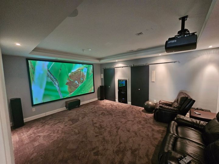 Home theater room with large wall screen, projector, recliners, and carpeted seating area