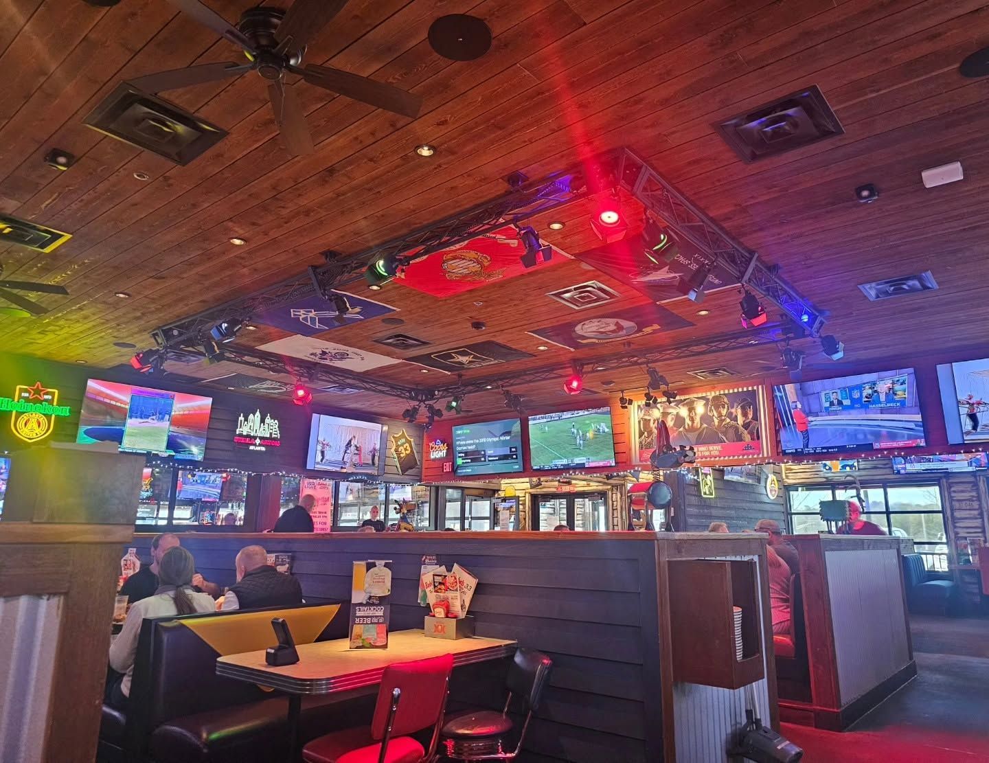 Dim sports bar with red-lit ceiling, many TVs, booths, and a few patrons seated inside.