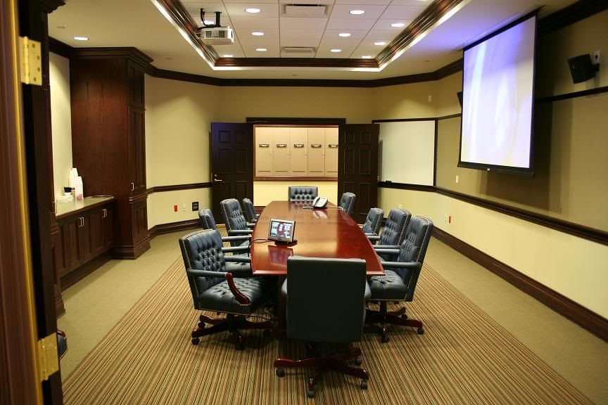 Conference room with long table, blue chairs, beige walls, and a projector screen.