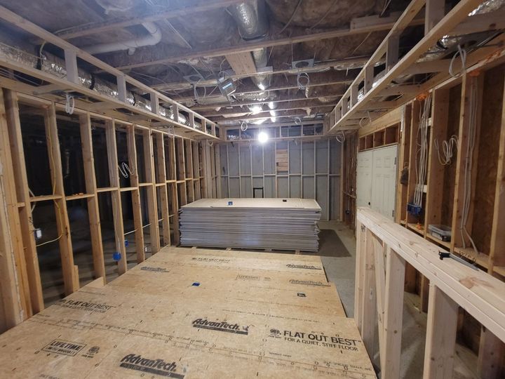 Unfinished basement framing with exposed studs, subflooring, and stacked insulation boards.