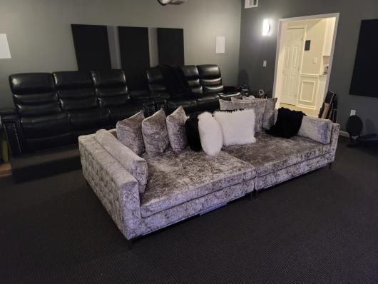 Modern living room with a gray sectional sofa, black walls, and a doorway in the background