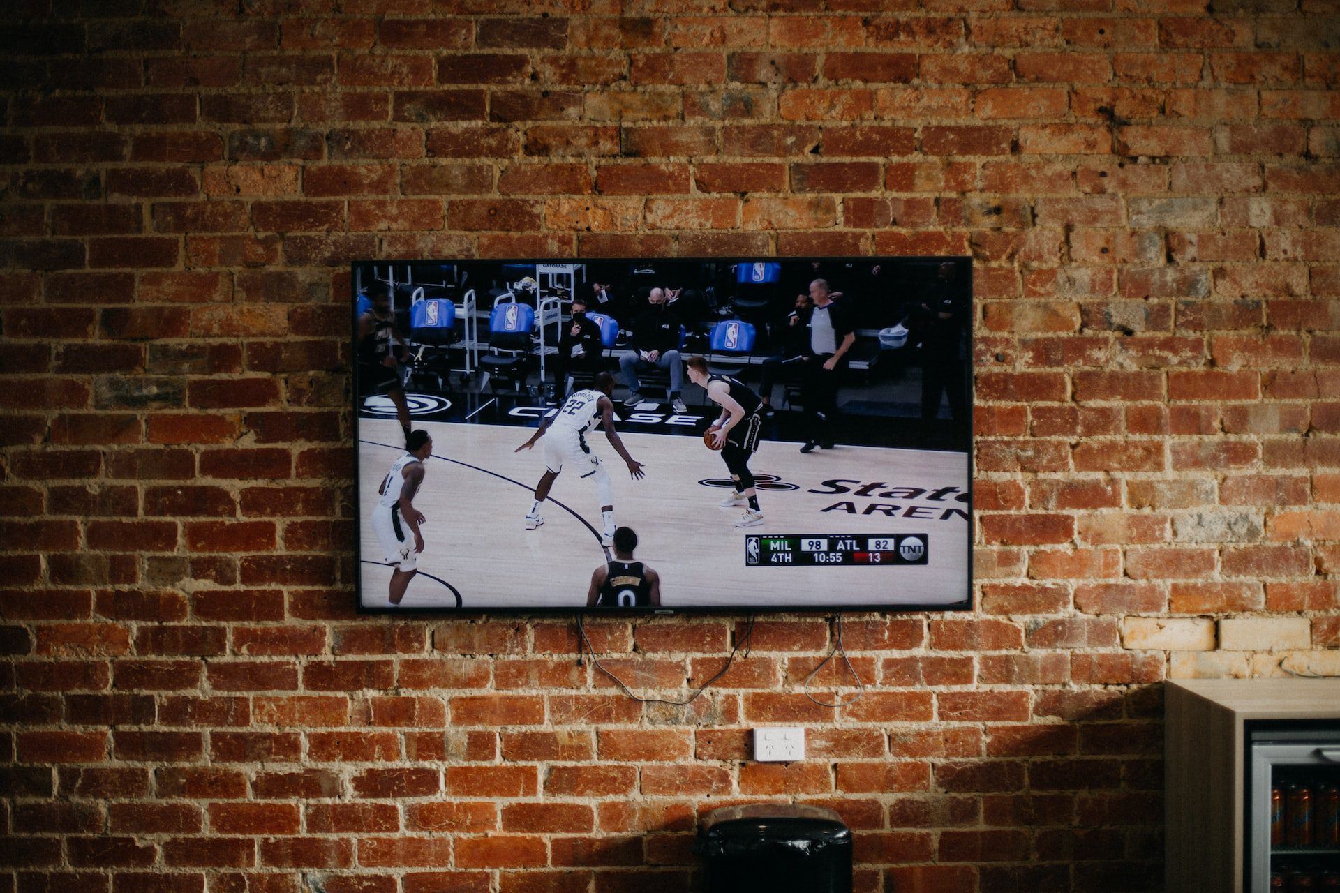 Wall-mounted TV showing a basketball game against a brick wall in a room