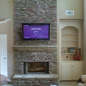 Stone fireplace wall with mounted TV above a fireplace and built-in shelves beside it