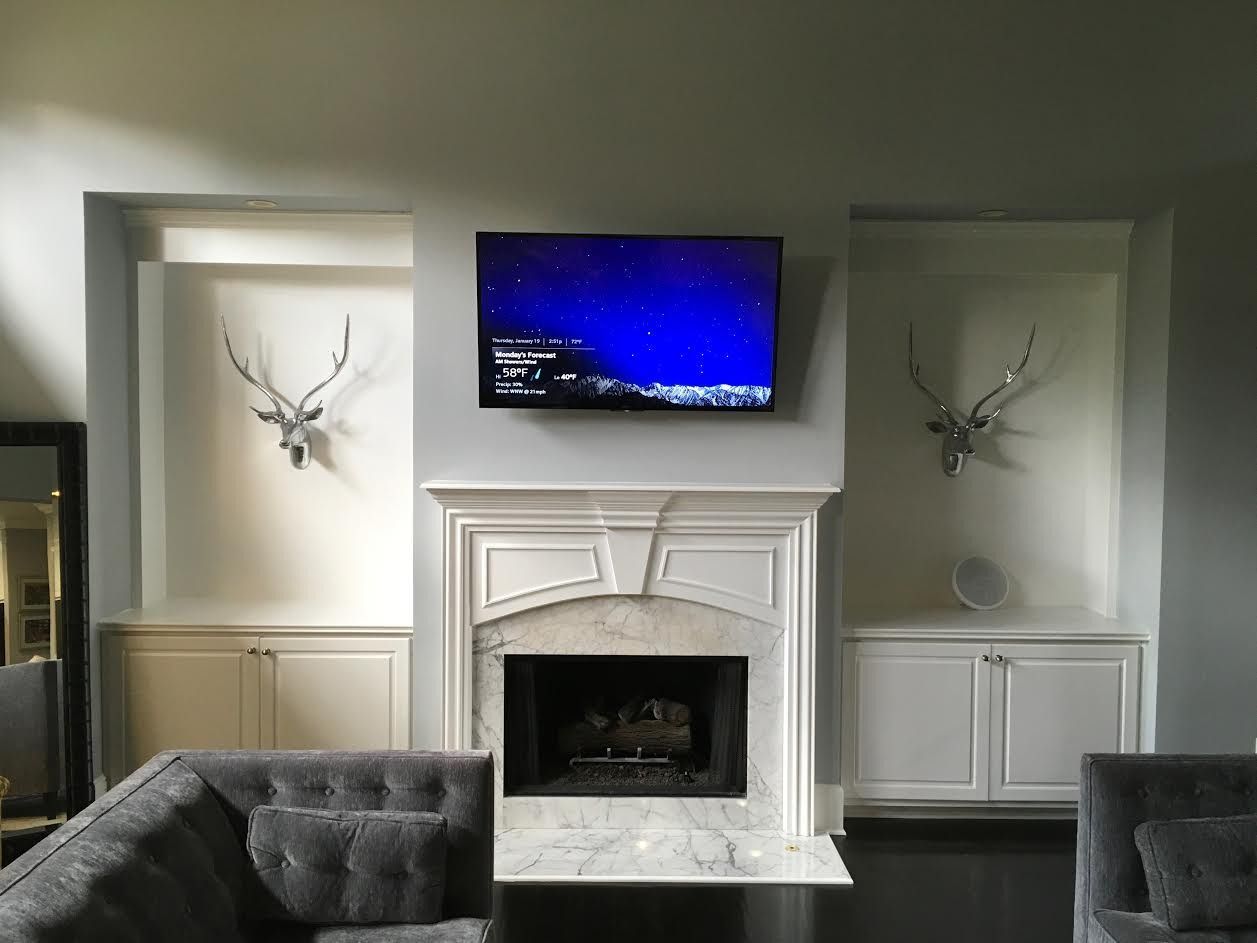 Living room with white fireplace, mounted TV, and antler wall art, framed by dark sofas.