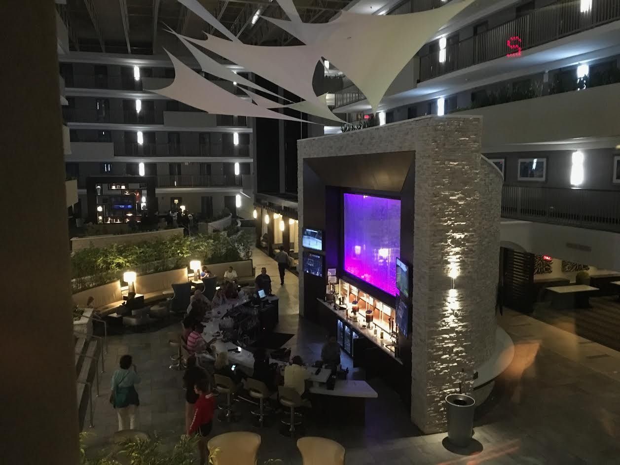 Hotel atrium with people gathered around a glowing purple central screen and seating areas below balconies