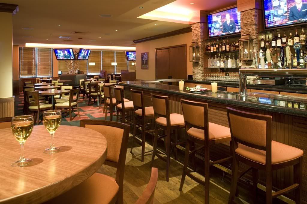 Empty bar and restaurant interior with warm lighting, tables, stools, and TVs on the wall