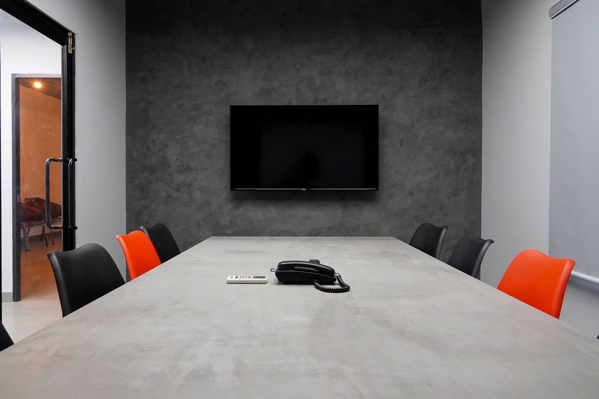 Modern conference room with a large table, wall-mounted TV, and black chairs with orange cushions