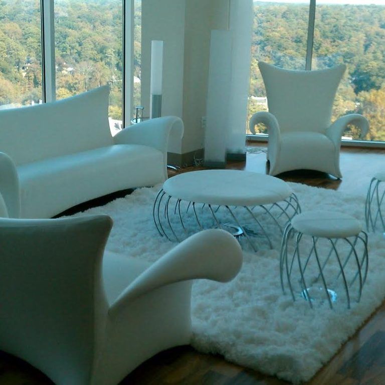 Modern white lounge with sculptural chairs, round tables, and fluffy rug by large windows.